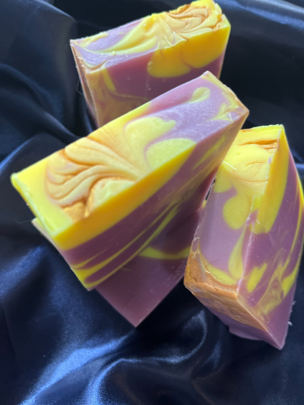 Handmade soap bars stacked, purple and yellow marbled colors with decorative swirl on front