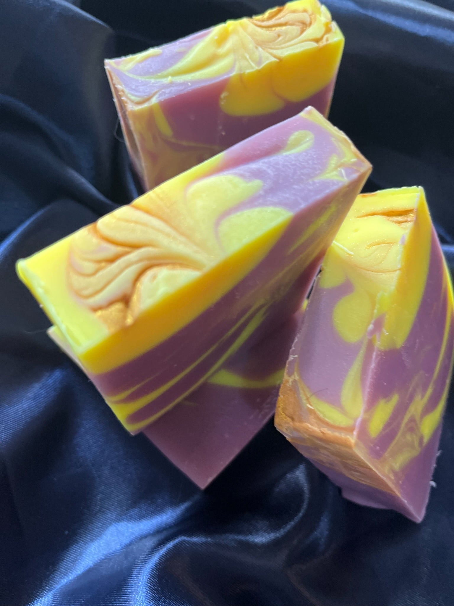 Handmade soap bars stacked, purple and yellow marbled colors with decorative swirl on front