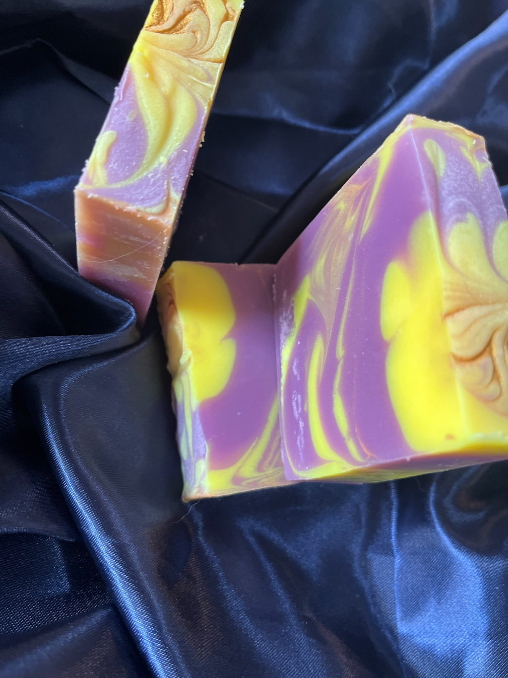 Purple and yellow marbled soap bars with curved seam line and embossed swirl on the right