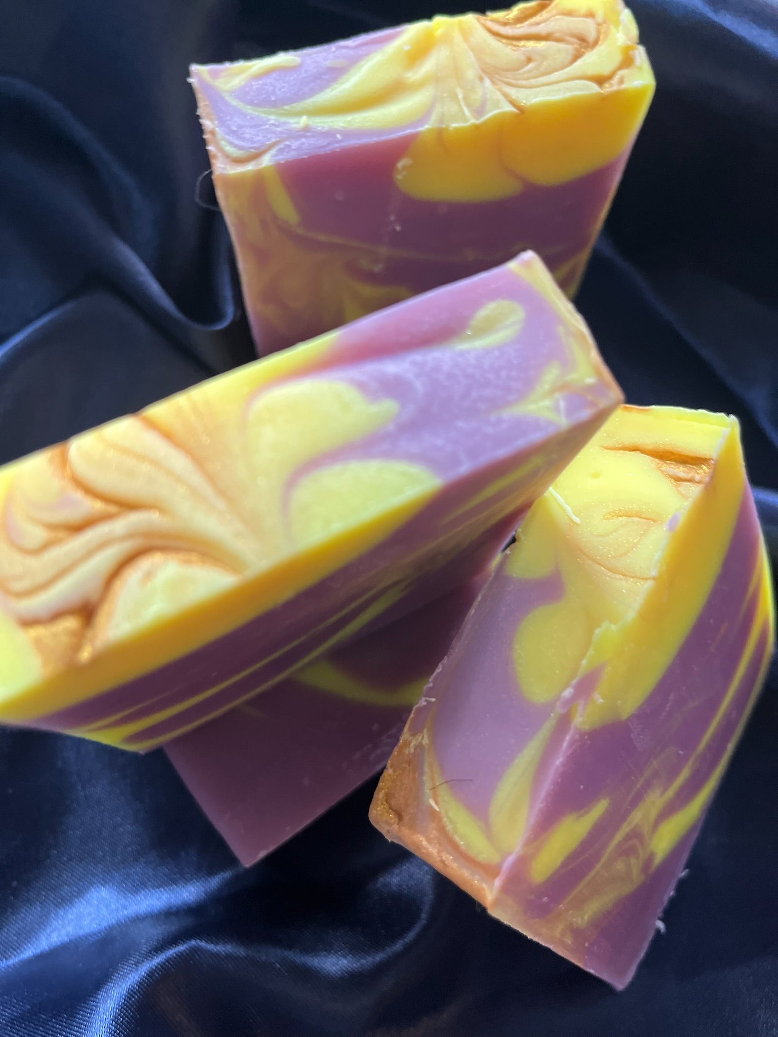 Handmade soap bars with purple base and yellow top, marbling streaks and carved swirl