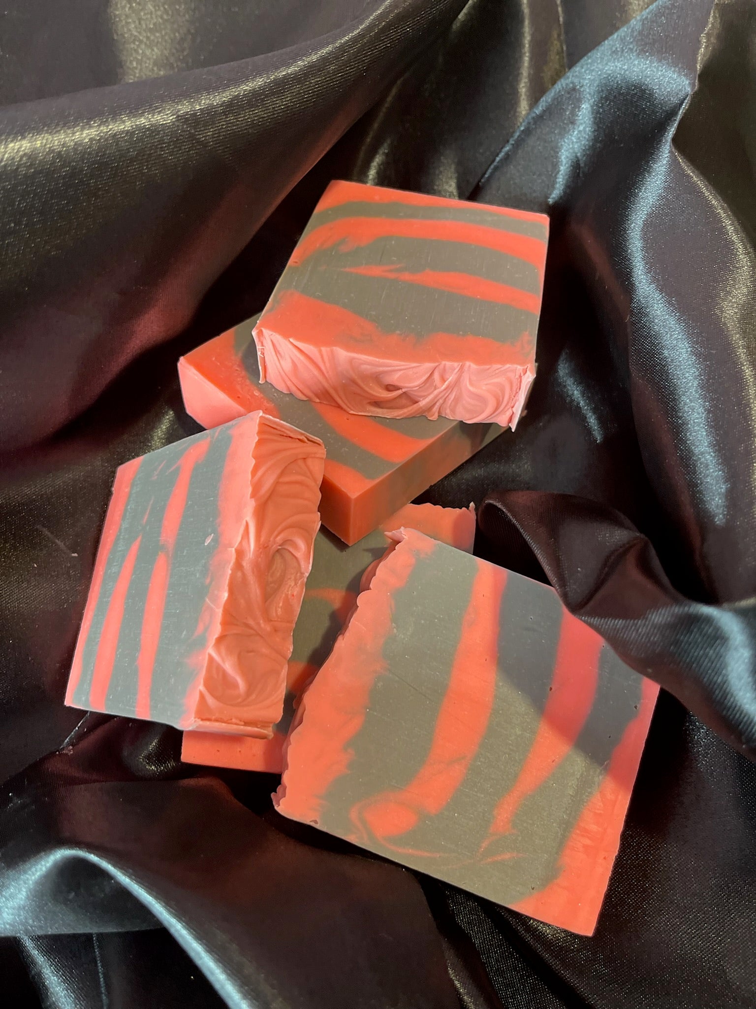 Assorted coral and gray striped soap bars arranged on dark satin